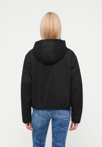 Μαύρο κοντό μπουφάν με κουκούλα, με μακριά μανί κια και ελαστική μέση. Συνδυάζεται με μπλε τζιν με σχέδια.