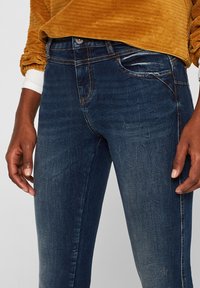 Jeans azul oscuro de corte slim, con un diseño clásico de cinco bolsillos, ligeras marcas de desgaste y detalles de costura en contraste.
