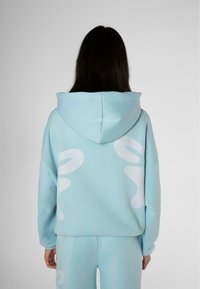 Felpa blu con cappuccio, caratterizzata da grandi motivi astratti bianchi sul retro. Realizzata in materiale morbido con maniche e corpo dalla vestibilità ampia.