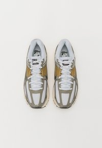 Ténis Nike Vomero com um cabedal em malha branca, detalhes em verde oliváceo e elementos refletivos. Apresenta atacadores brancos planos e língua acolchoada.