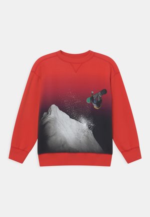 Sweatshirt rouge avec un design dégradé, mettant en avant un snowboarder noir et blanc sautant au-dessus d'un sommet enneigé, montrant texture et couleurs vives.
