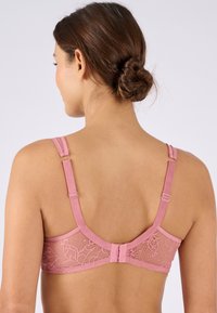 Reggiseno rosa in pizzo con spalline regolabili, fascia liscia e intricati motivi floreali sul retro. Presenta una chiusura a gancio e occhiello.