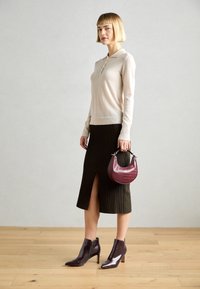 Beiger Langarm-Polo-Pullover, gerippter brauner Midirock mit seitlichem Schlitz, burgunderfarbene Handtasche mit Krokoprägung und dunkle Absatz-Ankle-Boots.