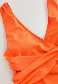 Enhelad baddräkt i stark orange, tillverkad av slät, elastisk tyg med en djup v-ringning och rynkade detaljer vid axlarna.