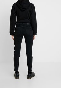 Svart denim skinny jeans med fem fickor, hög midja och subtila sömmar, kombinerat med en svart huvtröja och svarta skor.