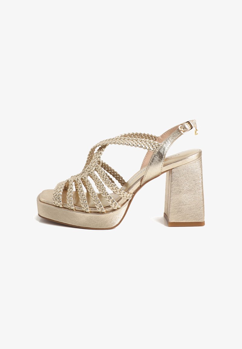 Guldsandal med høje hæle med flettede stropper, åben tå og en tykkere, firkantet hæl. Glat metallisk tekstur med en platåsål.