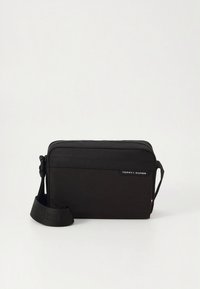 Black Tommy Hilfiger crossbody bag with adjustable strap and front zipper pocket on a plain white background.
