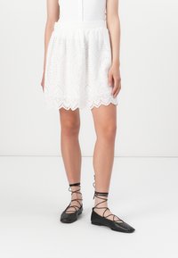 White eyelet skirt with scalloped hem details, paired with black flat shoes featuring crisscross ankle ties and a sleek design.