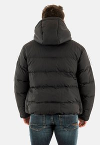 Chaqueta de plumas negra con capucha, diseño acolchado y paneles voluminosos. Presenta rayas de color claro en las mangas y una textura suave.