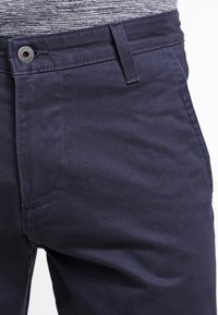 Granatowe spodnie bawełniane o gładkiej fakturze. Wyposażone w zapięcie na guzik oraz standardowe kieszenie z przodu. Klasyczny fason.