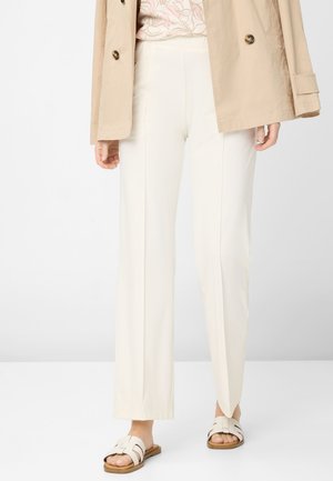 Pantalons taillés de couleur crème avec une coupe droite, associés à une veste beige et des sandales légères. Tissu lisse avec un léger éclat.