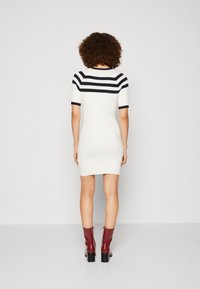 Robe en maille crème avec des rayures horizontales bleu marine sur les épaules et les manches courtes, présentant une silhouette ajustée et une texture côtelée subtile.