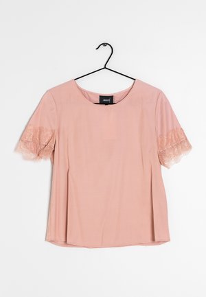 Lyserød kortærmet bluse med rund halsudskæring og blondekant på ærmerne. Glat tekstur, blødt stof, og en løst designet pasform.
