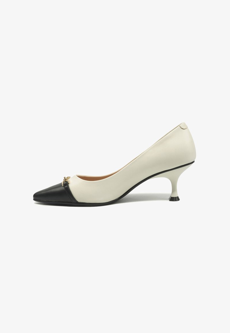 Zapato de tacón bajo para mujer en blanco y negro bicolor, con punta afilada y pequeño adorno dorado decorativo en la parte delantera.