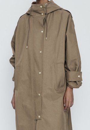 Beige, long hooded coat made from a soft, smooth fabric. Features snap buttons, adjustable drawstrings, and two large front pockets.