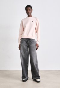 Világos rózsaszín pulóver kerek nyakkivágással és bordás mandzsettával, ami széles szárú szürke farmerral van párosítva. Figyelemre méltó fekete platform cipők texturált talppal.