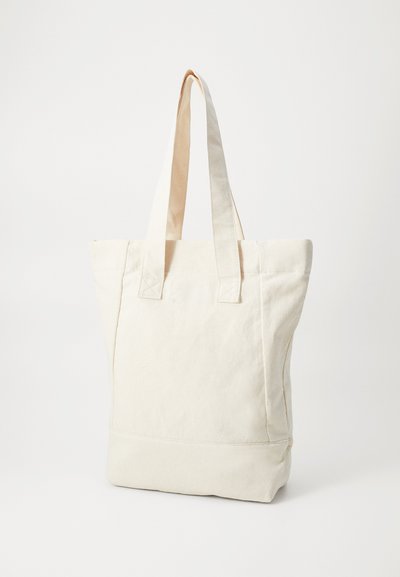 Geantă tote din pânză de culoare albă-cretă, cu două mânere pentru umăr, formă rectangulară și detalii de cusătură vizibile. Textură netedă și design minimalist.