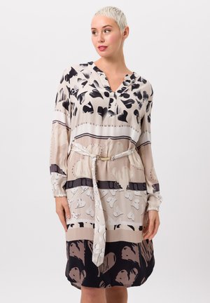 Crème en zwart gemusterd jurk met een V-hals, lange mouwen en een ceintuur in de taille. Bevat abstracte ontwerpen en gevarieerde kleurvlakken.