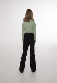 Pantaloni neri a zampa d'elefante con vita alta, abbinati a un top a maniche lunghe a coste di colore verde chiaro. Tessuto liscio con silhouette aderente.