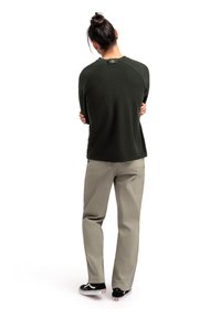 Camicia a maniche lunghe verde scuro con maniche raglan, abbinata a pantaloni beige chiaro e sneakers nere con suole bianche, vista da dietro.