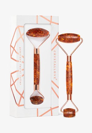 Rouleau facial en ambre avec un cadre en métal rose doré, présenté dans une boîte au design géométrique. Le rouleau présente une surface polie et texturée.