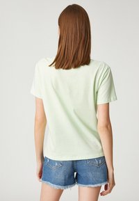 Jasnozielony bawełniany t-shirt z krótkimi rękawami, okrągłym dekoltem i luźnym krojem, połączony z dżinsowymi szortami z postrzępionymi brzegami.