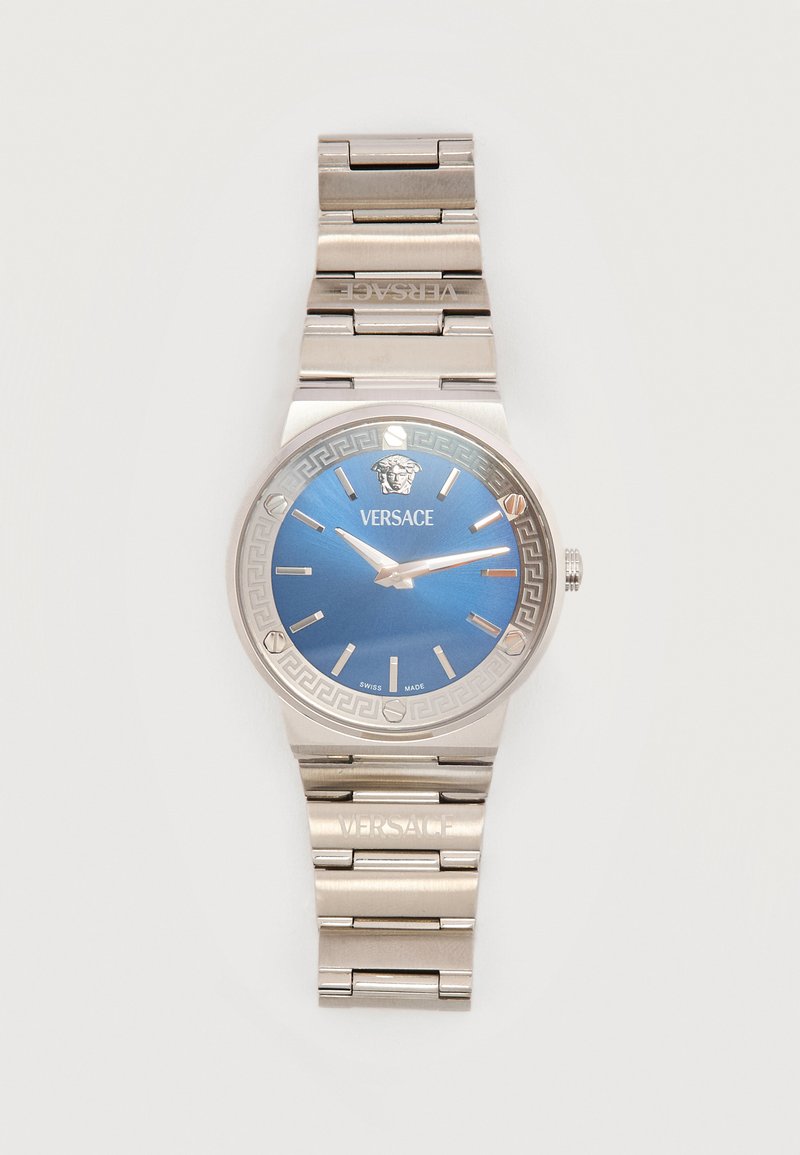 Ασημένιο μεταλλικό ρολόι χειρός Versace με μπλε καντράν, ασημένιους δείκτες ώρας και το λογότυπο Μέδουσας στις 12 η ώρα, μεταλλικό μπρασελέ με συνδέσμους χαραγμένο με το όνομα Versace.
