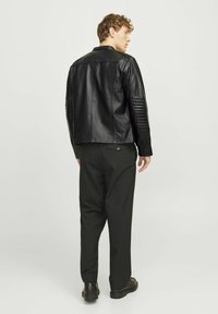 Jachetă din piele neagră cu detalii cu model matlasat pe umeri, combinată cu pantaloni negri și pantofi negri, văzută din spate.