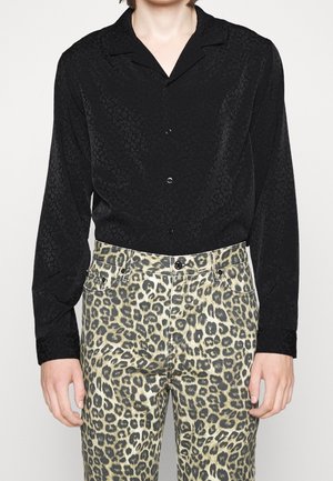 Osoba ubrana w czarną koszulę z długim rękawem zapinaną na guziki z subtelnym nadrukiem w panterkę oraz spodnie z nadrukiem w panterkę z wysokim stanem.