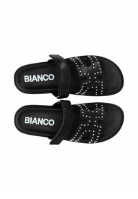 Sandales noires avec une bride ornée de rivets en argent, au design plat et logo sur la semelle intérieure. Style minimaliste et bride ajustable.