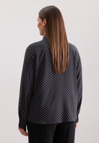 Zwarte blouse met lange mouwen en witte stippen, met een klassieke kraag en een ontspannen pasvorm, gemaakt van een soepele stof, met knoopmanchetten.