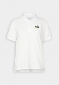 Valkoinen polo-paita, jossa on kaulus ja vasemmalla puolella pieni monivärinen kirjailtu kuvio. Valmistettu pehmeästä puuvillamateriaalista.