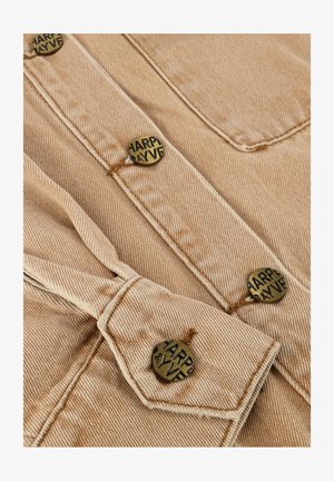 Beige spijkerjack met een bruine stiksels en ronde metalen knopen met de gravure "HARPER & YVE."