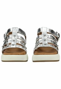 Stříbrné metalické sandály s více horizontálními popruhy, metalickými hroty a bílou gumovou podrážkou. Mají sponu na boku.