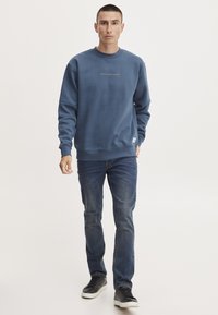 Blauwe sweatshirt met een ronde halslijn, voorzien van een klein gouden logo op de borst. Draag het met donkere jeans en zwarte sneakers.