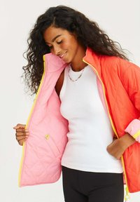Prošívaná bunda s jasně oranžovým vnějškem a měkkou růžovou podšívkou, se žlutým zipem a akcentovými detaily.