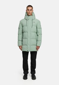 Svetlozeleni zimski plašč s podlogo, visokim ovratnikom, zadrgo na sprednji strani in nastavljivimi vrvicami. Ima stranske žepe in sproščen kroj.