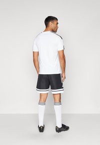 Hvid atletisk skjorte med sorte accenter, sorte shorts med hvide striber, hvide sokker med grå bånd og sorte fodbold støvler.