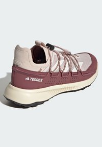 Chaussure de randonnée Terrex avec un dessus rose clair, des accents bordeaux foncé, une finition texturée, des panneaux en mesh, un système de laçage élastique et une semelle durable.