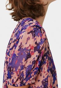 Blus med blommönster som har korta puffärmar, rund halsringning och en blandning av rosa, lila och blå nyanser. Tillverkad av lättviktig tyg.