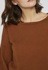 Pull en laine marron avec une texture douce et côtelée, un col large et une coupe décontractée, mettant en valeur un design simple mais élégant.
