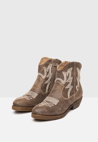 Bruna läderankelstövlar med dekorativ vit broderi, med en sidoglidare och en låg träklack. Texturerad, grov yta.