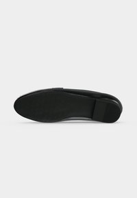 Semelle de chaussure formelle noire avec une surface antidérapante texturée et une section de talon côtelée, photographiée sur fond blanc uni.