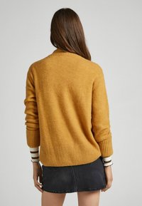 Pull jaune moutarde avec un ourlet et des poignets côtelés, fabriqué dans un matériau doux, assorti à une jupe en denim foncé. Vue de dos montrant la simplicité du design.