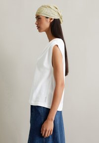 Witte katoenen mouwloze top met een losse pasvorm, met een ronde halslijn en een zijsplit. Draag met een blauwe spijkerrok, het model heeft lang haar.