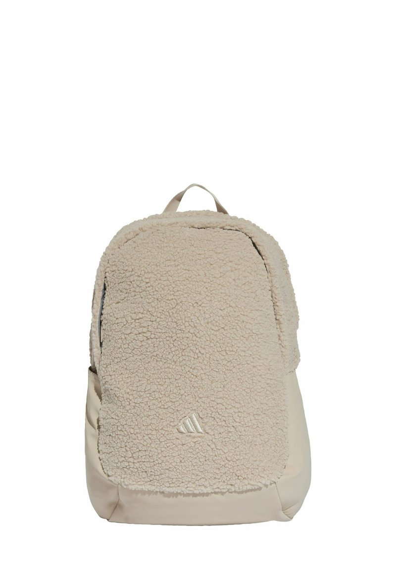 Mochila beige con un panel frontal de felpa suave, sección inferior lisa y un asa superior para llevar. Presenta un discreto detalle de logotipo en la parte inferior.