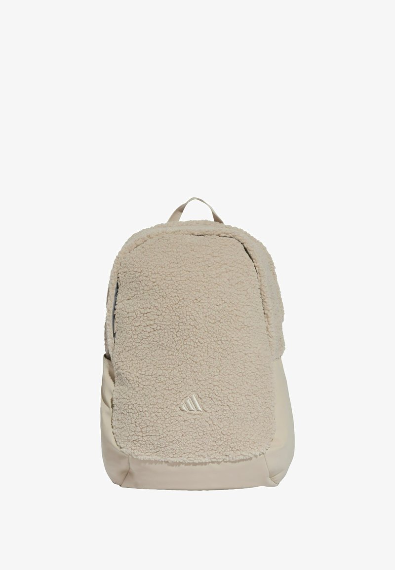 Beige backpack with a fuzzy fleece front panel, smooth lower section, and a top carry handle. Features subtle logo detail at the bottom.