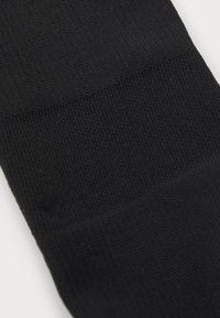 Chaussette noire avec un motif de tricot texturé, présentant trois sections distinctes avec des textures variées et une couleur uniforme tout au long.
