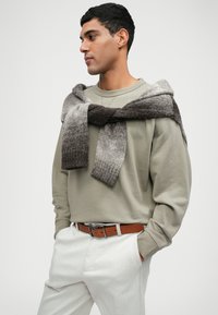 Šedá mikina v kombinaci se svetle šedými kalhotami. Pletený šátek v odstínech šedé leží přes ramena. Hnědý opasek dotváří celkový vzhled.