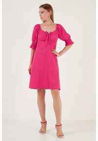 Pink, knee-length dress with a smocked neckline, puff sleeves, and a tie detail at the front. The fabric has a textured appearance.